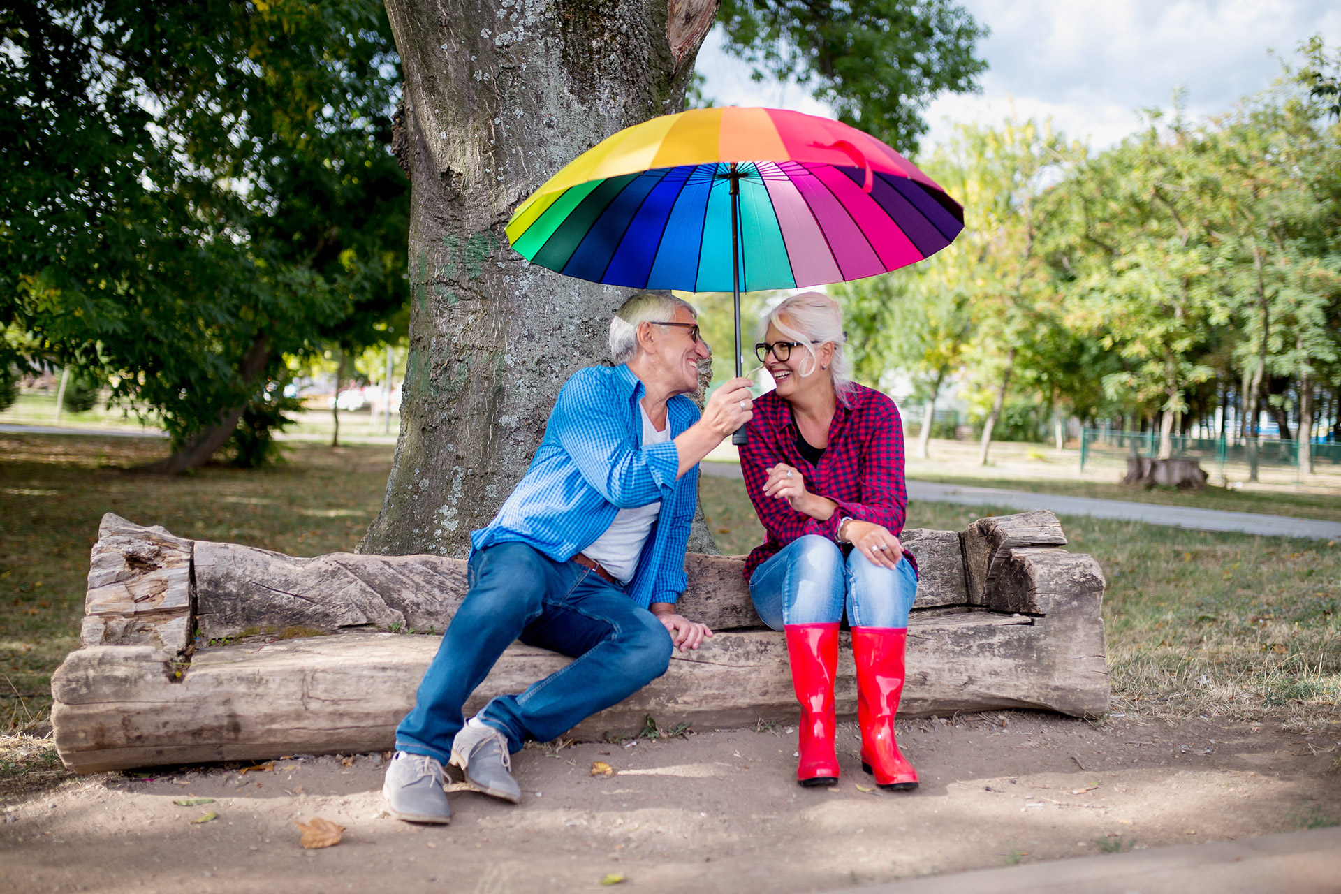 Ein Paar welches glücklich unter einem regenbogenfarbenen Regenschirm sitzt