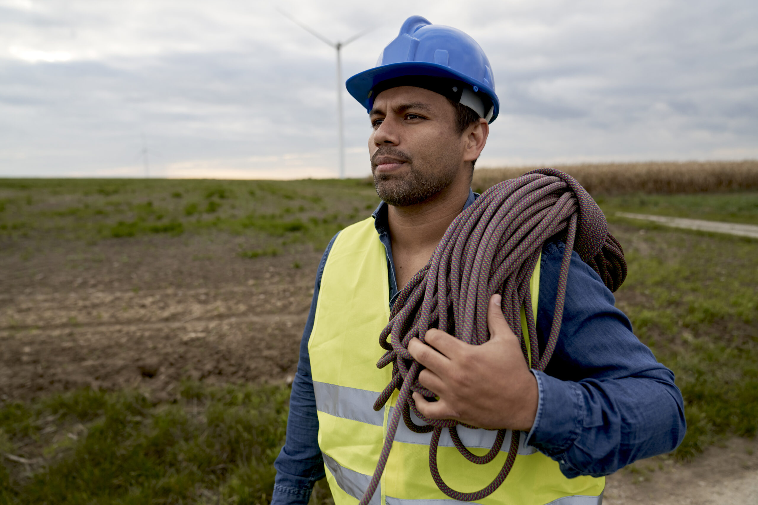 Latin male maintenance engineer carrying climbing rope and walking across the wind turbine
